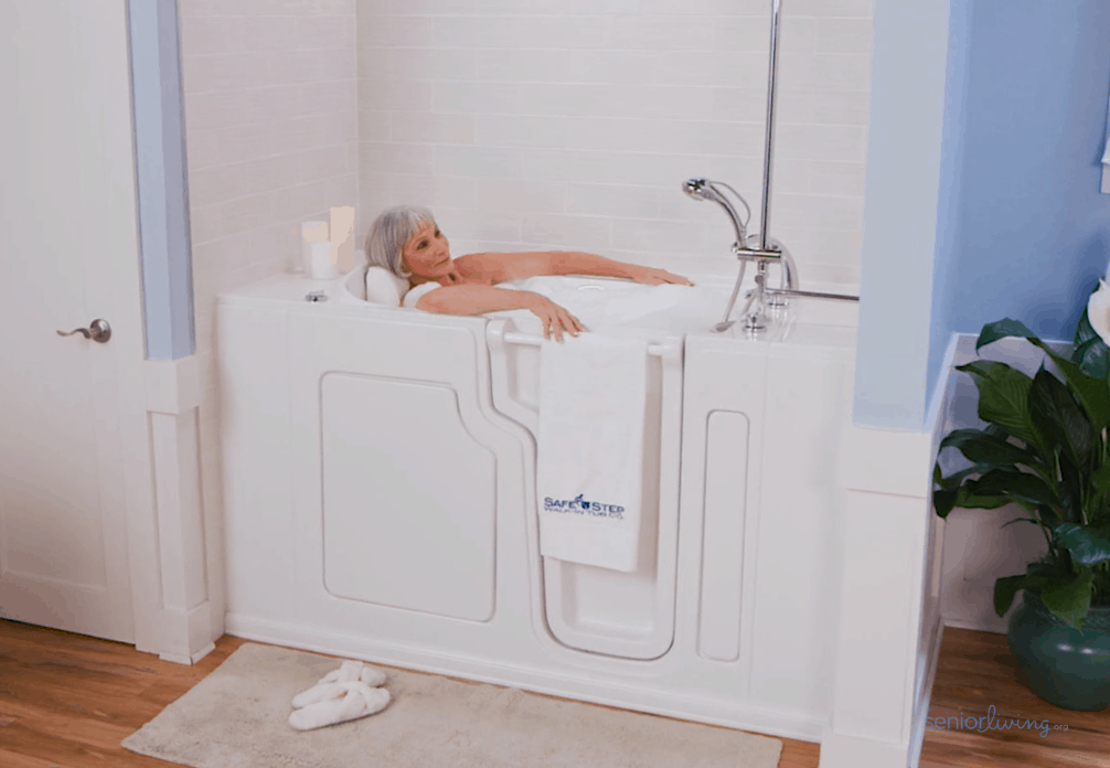 Senior woman relaxing comfortably in a white Safe Step walk-in tub with modern chrome fixtures in a bright, clean bathroom